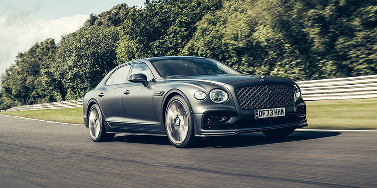 Bentley Hong Kong - Kam Lung Bentley Flying Spur Mulliner sedan front three quarter in dark grey paint driving dynamically by some trees on a track 