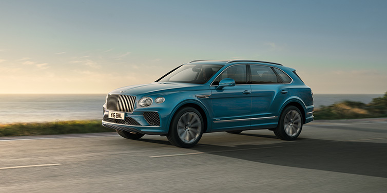 Bentley Hong Kong - Kam Lung Bentley Bentayga Azure SUV in Topaz blue paint driving dynamically by the ocean with 22 inch 10 spoke directional wheels 