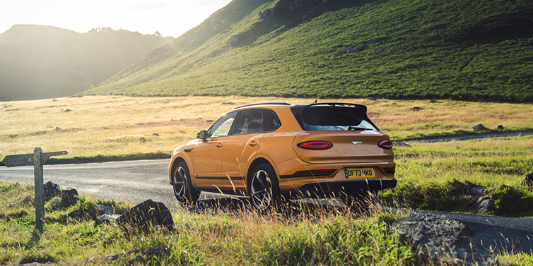 Bentley Hong Kong - Kam Lung Bentley Bentayga S SUV rear three quarter in Sunburst Gold paint on a road surrounded by green hills