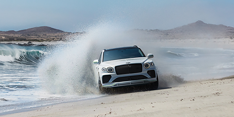 Bentley Hong Kong - Kam Lung Bentley Bentayga Speed SUV facing front in Snow Quarts Pearlescent white paint driving dynamically on beach