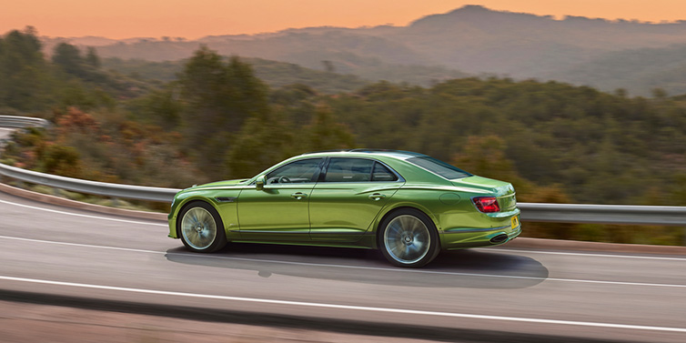 Bentley Hong Kong - Kam Lung Bentley Flying Spur Speed sedan side profile in Tourmaline Green paint driving dynamically on a mountain road at sunset