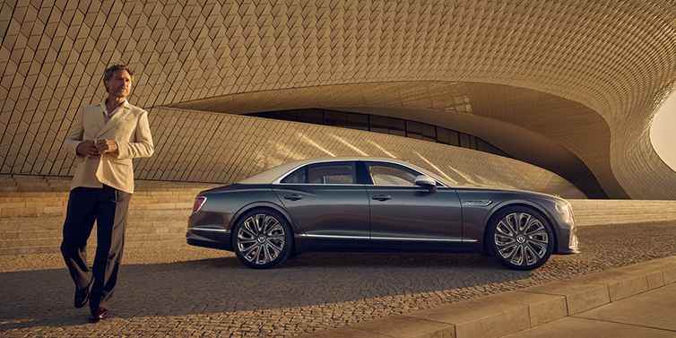 Bentley Hong Kong - Kam Lung Bentley Flying Spur Mulliner sedan in Rose Gold over Magnetic duotone paint parked by a curved wall with person in suit jacket standing on the left